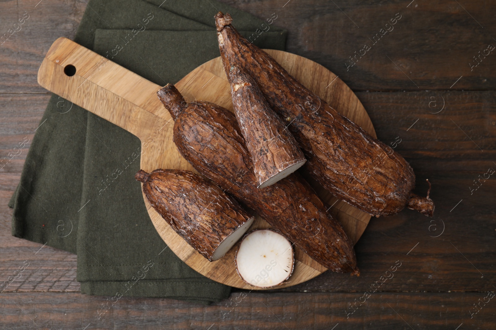 Photo of Whole and cut cassava roots on wooden table, top view