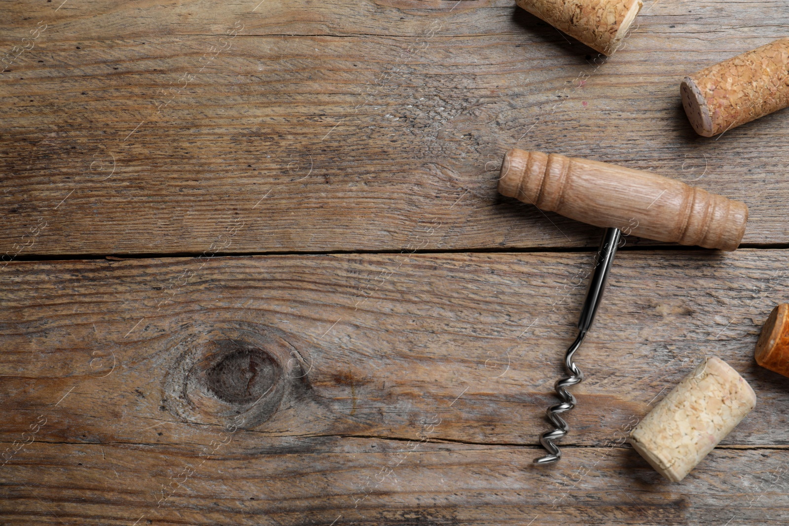 Photo of Corkscrew and wine corks on wooden table, flat lay. Space for text