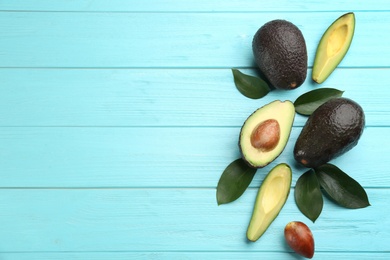 Whole and cut avocados with green leaves on turquoise wooden table, flat lay. Space for text