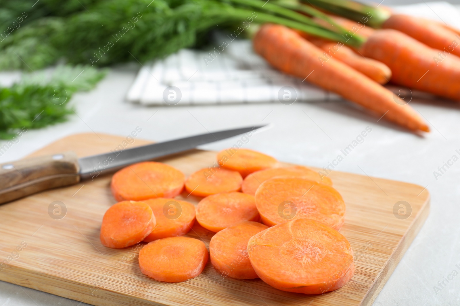 Photo of Wooden board with carrot slices and knife on light grey marble table, closeup