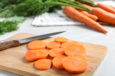 Photo of Wooden board with carrot slices and knife on light grey marble table, closeup