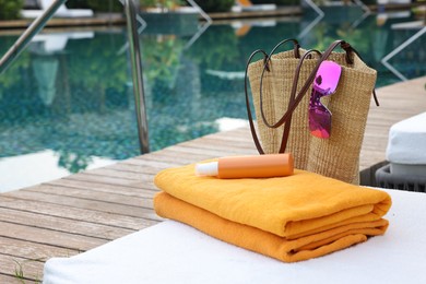 Photo of Wicker bag with beach accessories on sunbed near outdoor swimming pool, space for text. Luxury resort