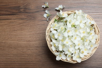 Photo of Wicker bowl with beautiful jasmine flowers on wooden table, flat lay. Space for text