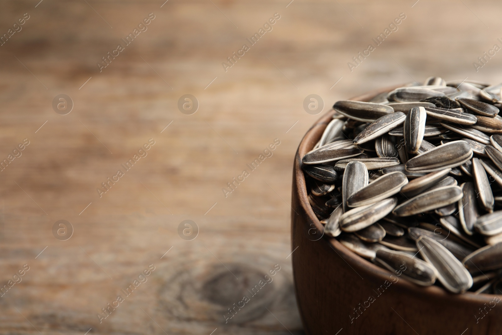 Photo of Raw sunflower seeds on wooden table, closeup. Space for text