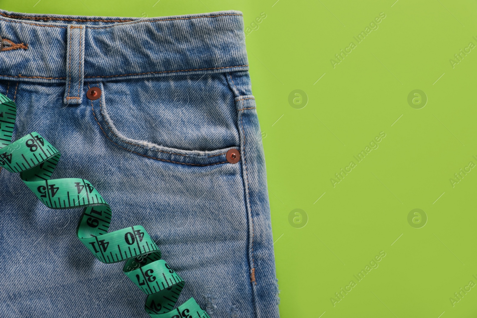 Photo of Jeans and measuring tape on light green background, top view with space for text. Weight loss concept