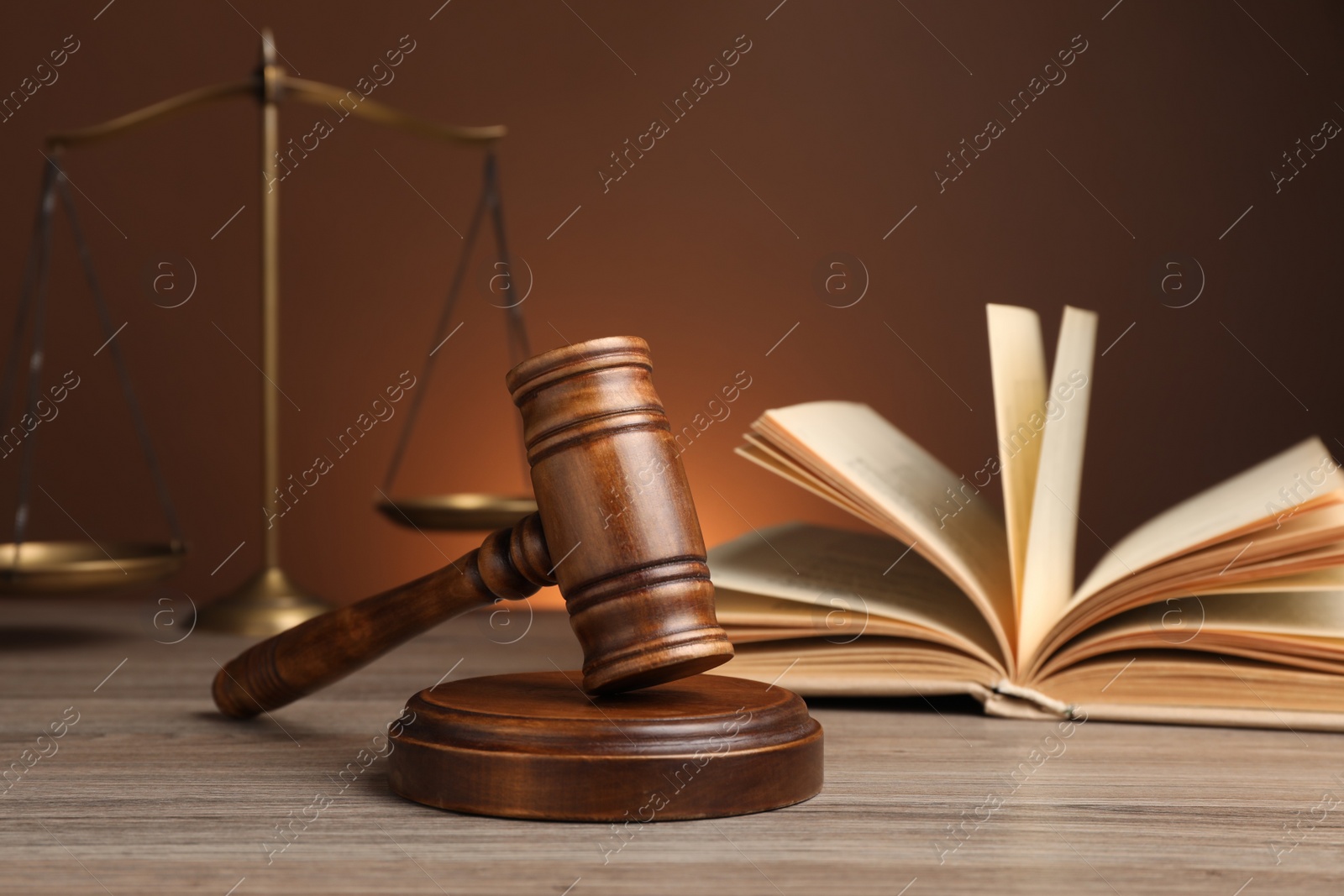 Photo of Judge's gavel with sound block, scales of justice and book on wooden table against brown background