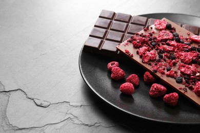 Photo of Plate and different chocolate bars with freeze dried fruits on slate table. Space for text