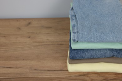 Photo of Stack of different folded clothes on wooden table near grey wall, above view. Space for text