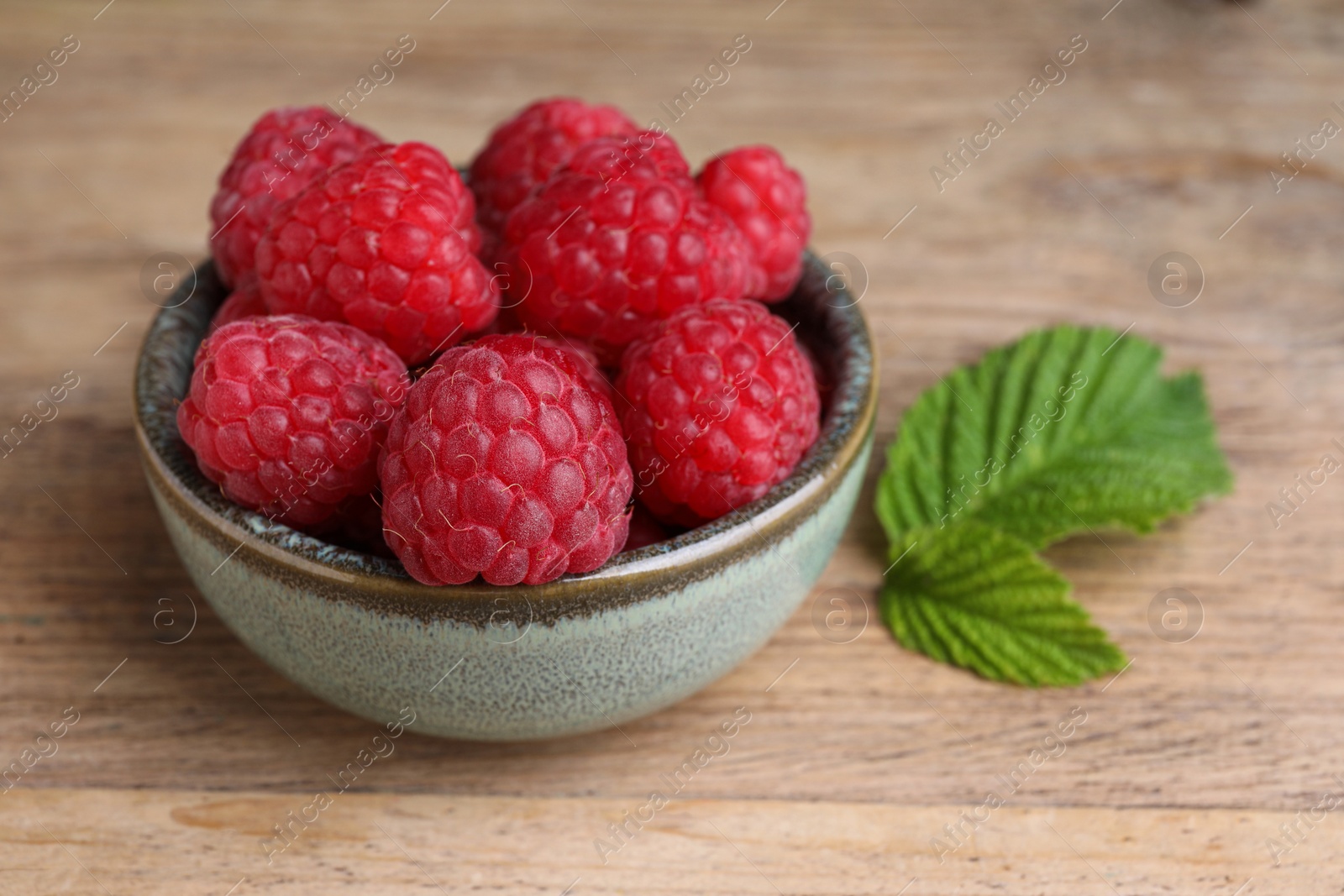 Photo of Tasty ripe raspberries and green leaves on wooden table, closeup