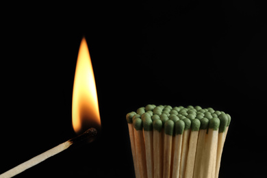 Photo of Burning match near unlit ones on black background, closeup