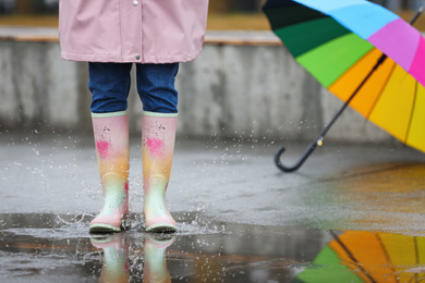 Photo of Woman in rubber boots walking outdoors on rainy day, closeup