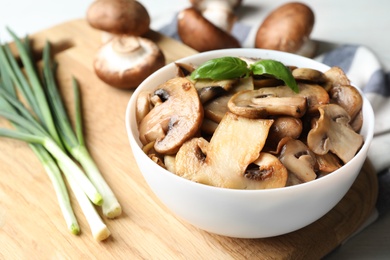 Photo of Delicious cooked mushrooms with basil in bowl on table