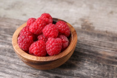 Photo of Tasty ripe raspberries in bowl on wooden table, space for text