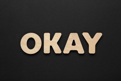 Photo of Word Okay made of wooden letters on black background, top view