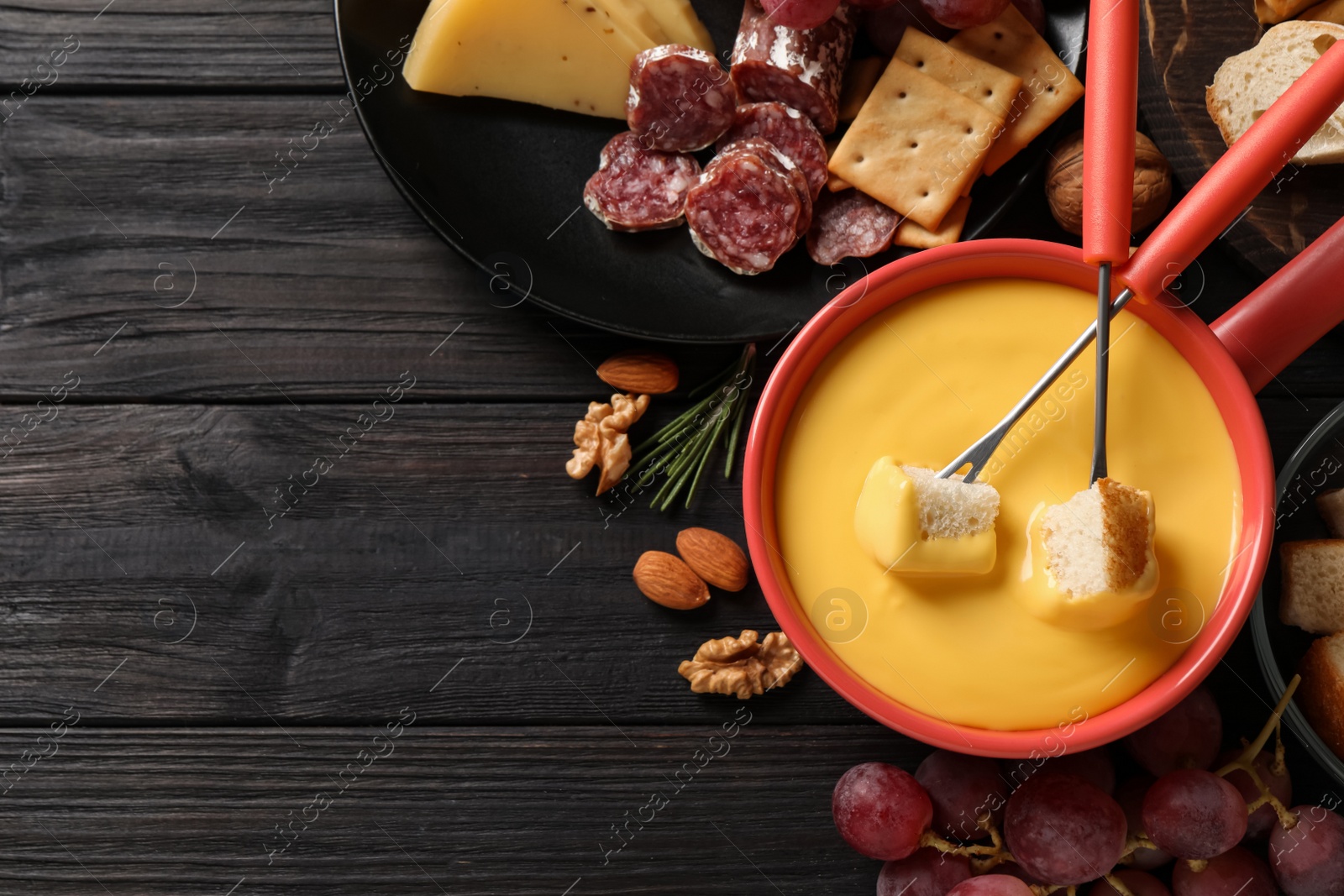 Photo of Pot of tasty cheese fondue and snacks on black wooden table, flat lay. Space for text