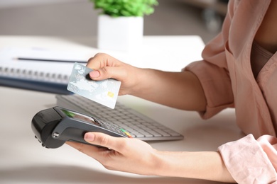 Woman using modern payment terminal at table indoors, closeup