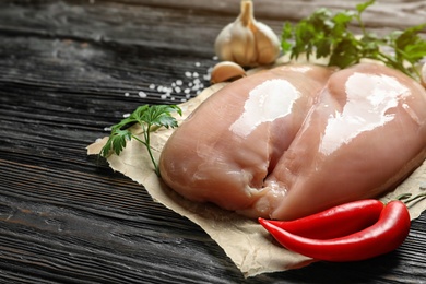 Photo of Raw chicken breasts, parsley and chili peppers on wooden table