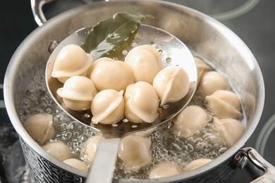 Photo of Closeup of dumplings on skimmer over stewpan with boiling water. Home cooking