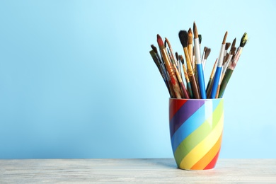 Holder with paint brushes on table against color background. Space for text