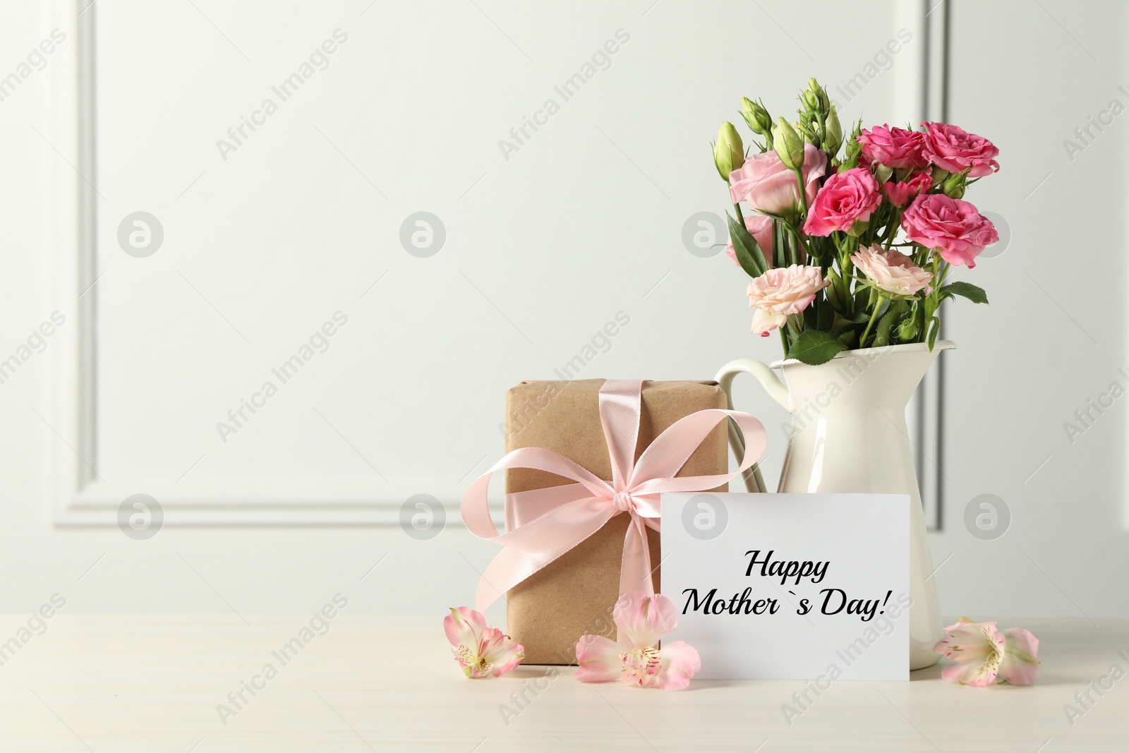 Image of Happy Mother's Day greeting card, gift box and bouquet of beautiful flowers on white wooden table