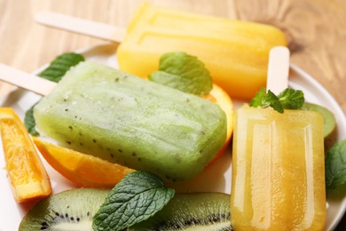 Photo of Plate of tasty orange and kiwi ice pops on table, closeup. Fruit popsicle