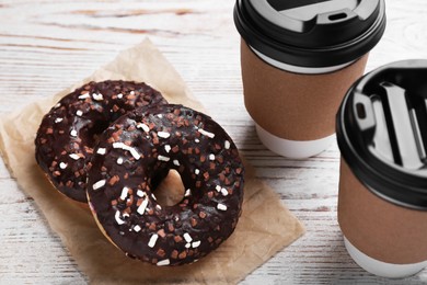 Tasty donuts and cups of hot drinks on white wooden table