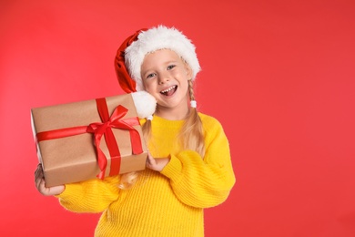 Photo of Happy little child in Santa hat with gift box on red background. Christmas celebration