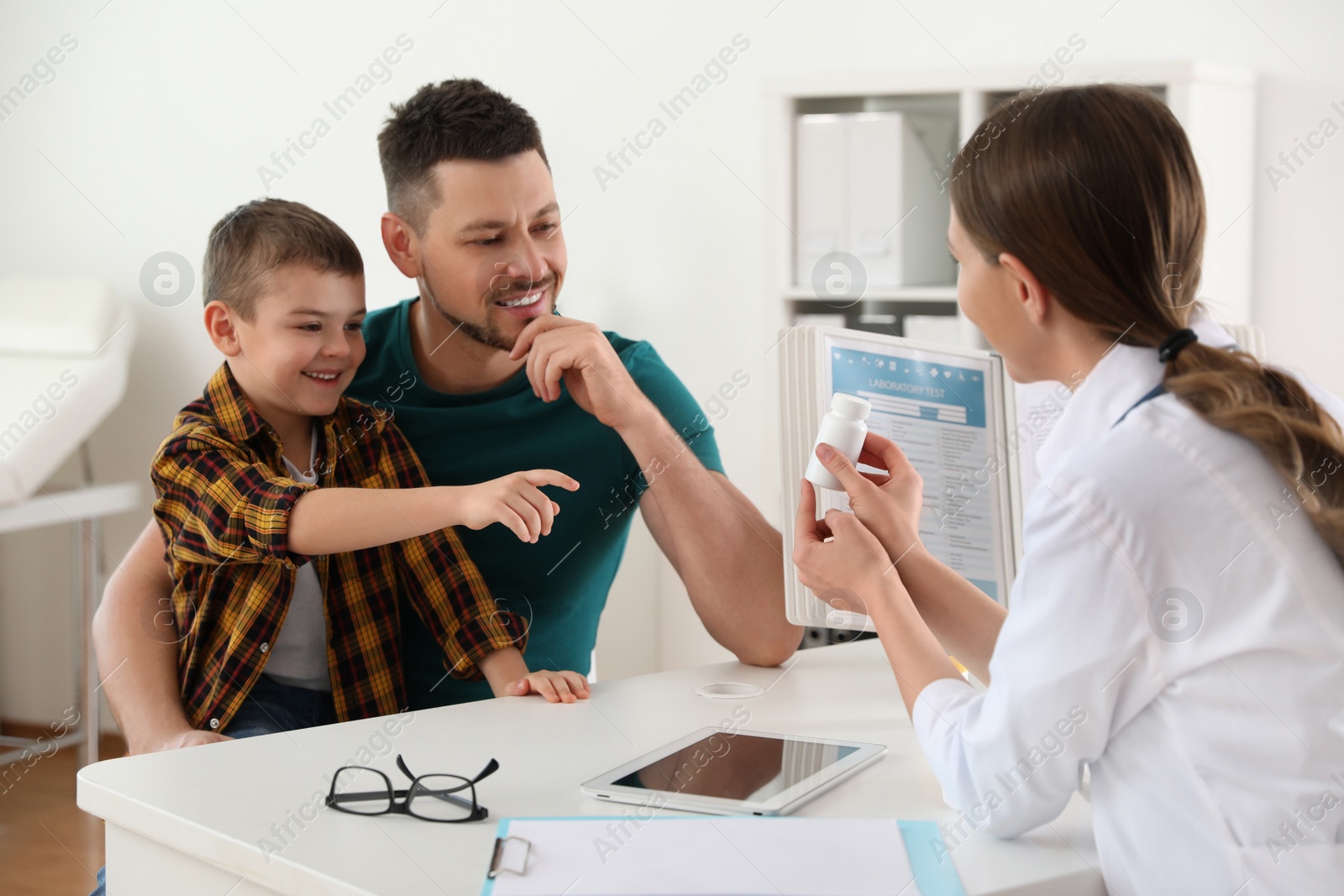 Photo of Father and son visiting pediatrician. Doctor working with little patient in hospital