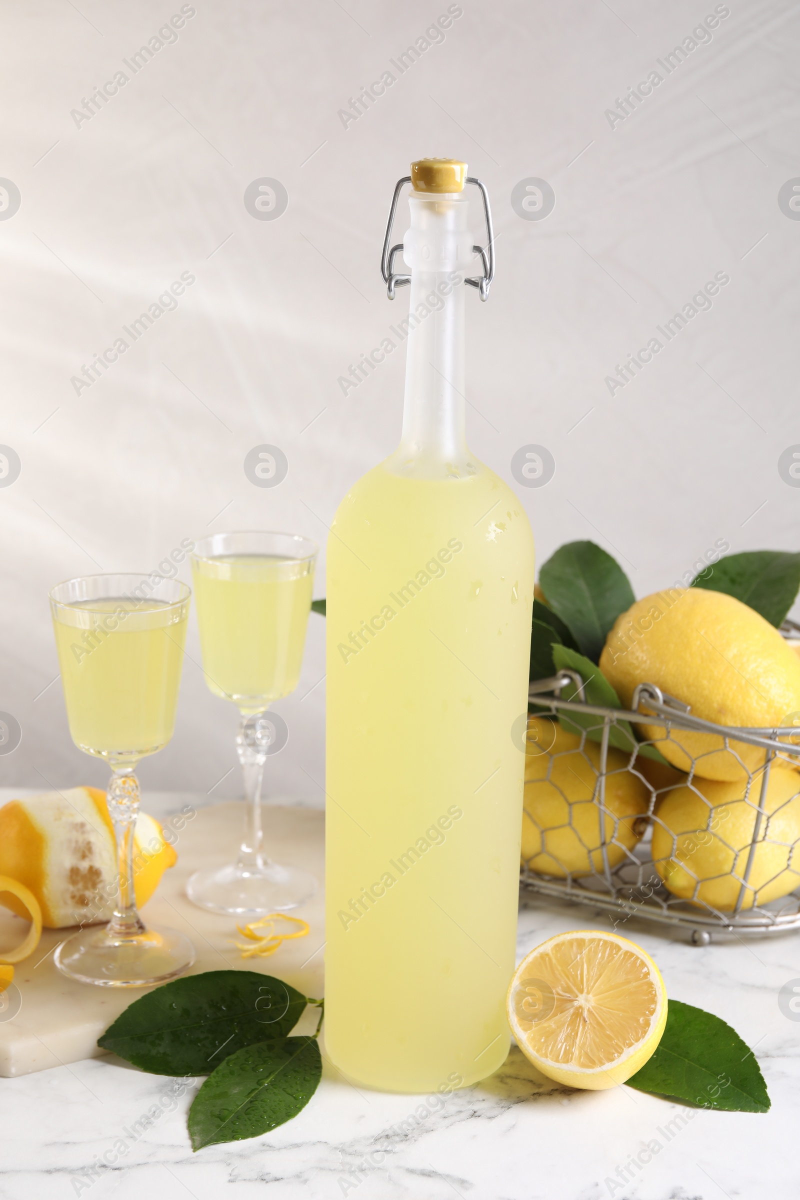 Photo of Tasty limoncello liqueur, lemons and green leaves on white marble table