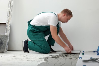 Photo of Worker installing ceramic tile on floor near wall