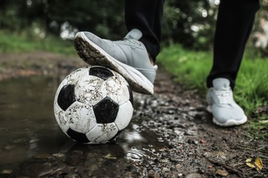 Photo of Man with dirty soccer ball in puddle outdoors, closeup