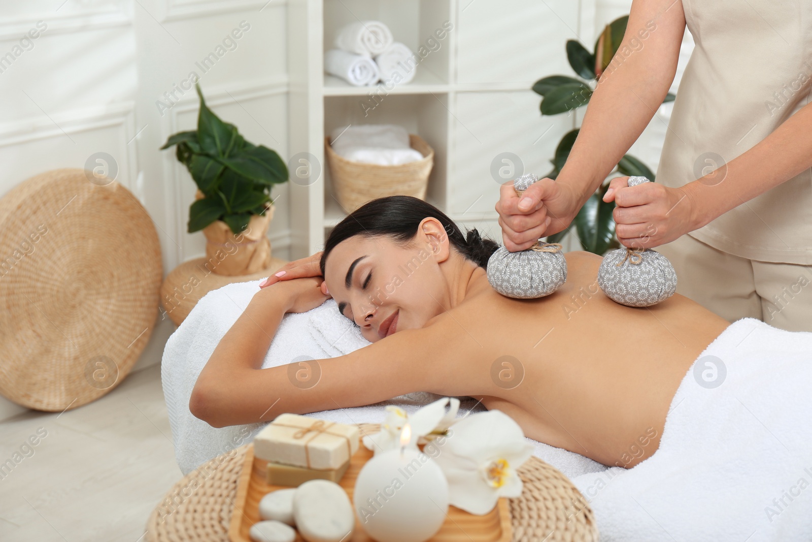 Photo of Young woman receiving herbal bag massage in spa salon