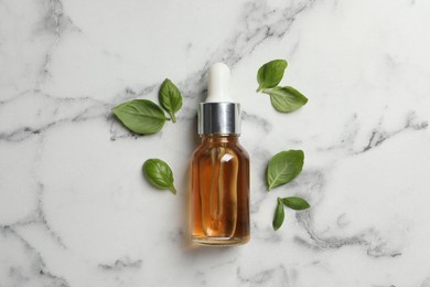 Photo of Bottle of essential basil oil and fresh leaves on white marble table, flat lay