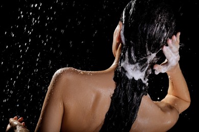 Photo of Young woman washing hair while taking shower on black background