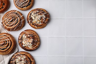 Photo of Sweet buns. Delicious rolls with raisins and toppings on white tiled table, flat lay. Space for text