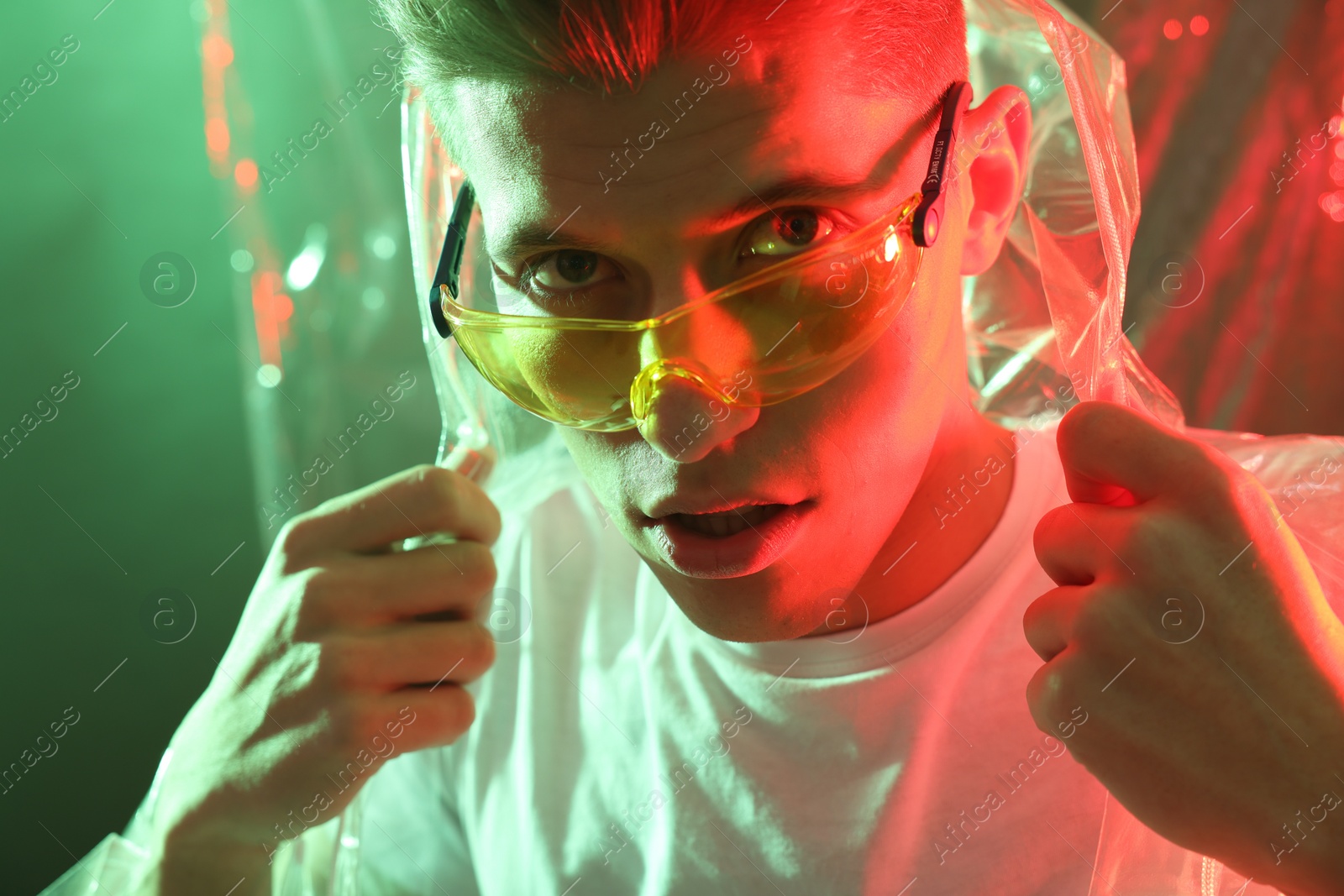 Photo of Stylish young man wearing clear coat and glasses in neon lights, closeup