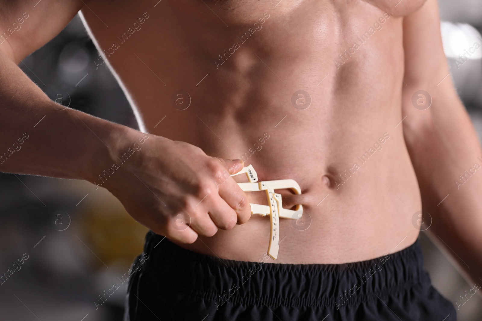 Photo of Man measuring body fat layer with caliper indoors, closeup