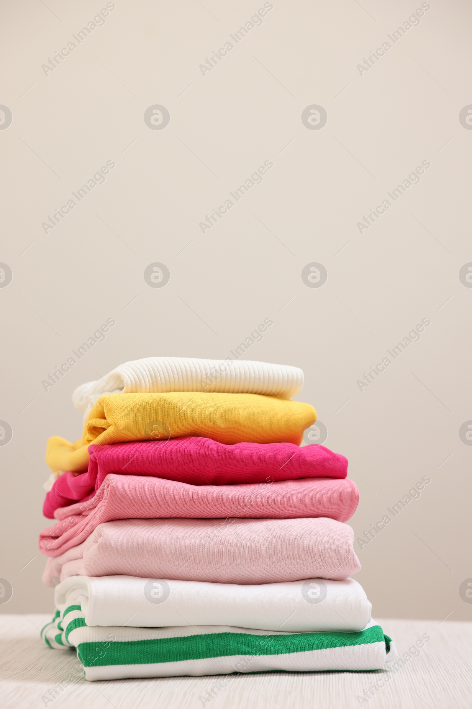 Stack of folded clothes on wooden table against beige background, space for text Photo of Stack of folded clothes on wooden table against beige background, space for text