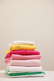 Photo of Stack of folded clothes on wooden table against beige background, space for text