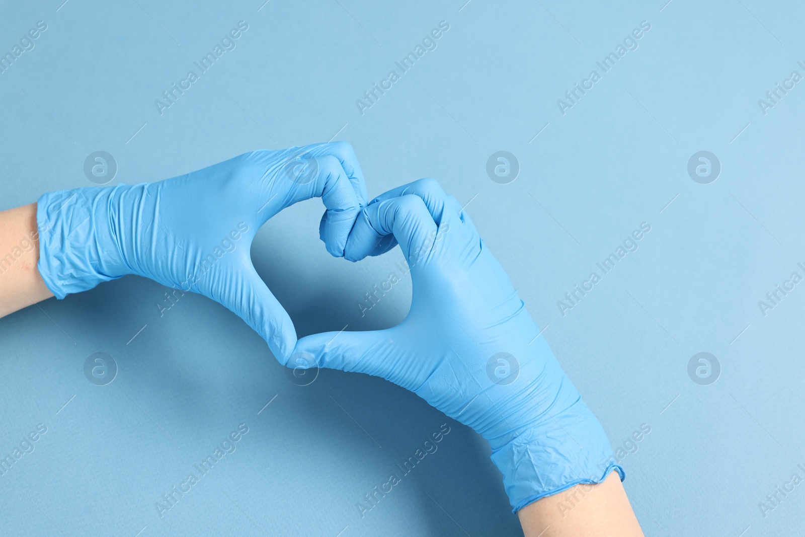 Photo of Doctor showing heart gesture with hands on light blue background, top view