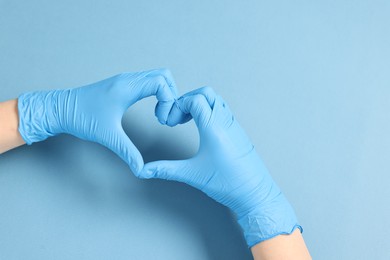 Doctor showing heart gesture with hands on light blue background, top view