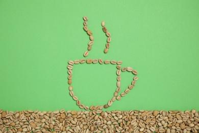 Cup of hot drink, composition made with coffee beans on green background, flat lay