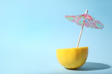 Photo of Creative image of summer cocktail made with lemon and small paper umbrella on light blue background, space for text