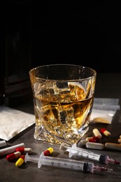 Photo of Alcohol and drug addiction. Whiskey in glass, syringes, pills, pills and cocaine on grey table