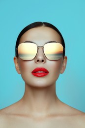 Image of Attractive woman in stylish sunglasses on light blue background. Sea sunset reflecting in lenses