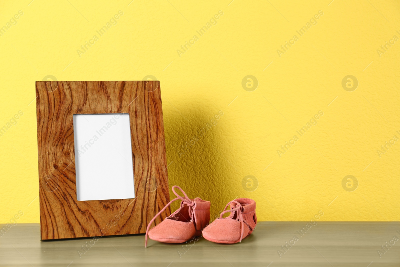 Photo of Photo frame and bootees for baby room interior on table near yellow wall