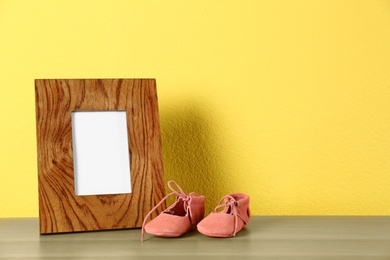 Photo of Photo frame and bootees for baby room interior on table near yellow wall