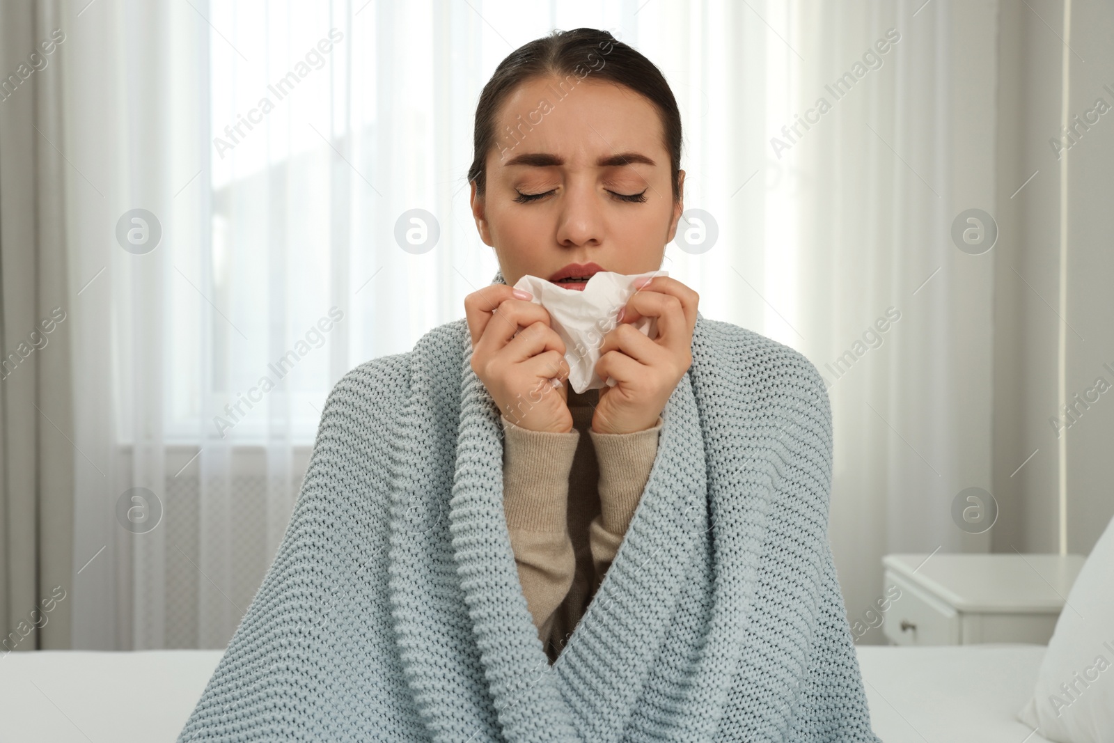 Photo of Sick young woman with tissue wrapped in knitted plaid at home