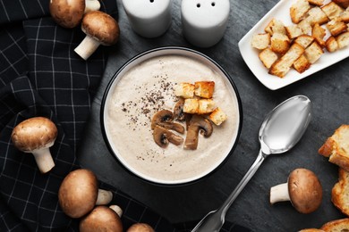 Photo of Delicious cream soup with mushrooms and croutons on black table, flat lay