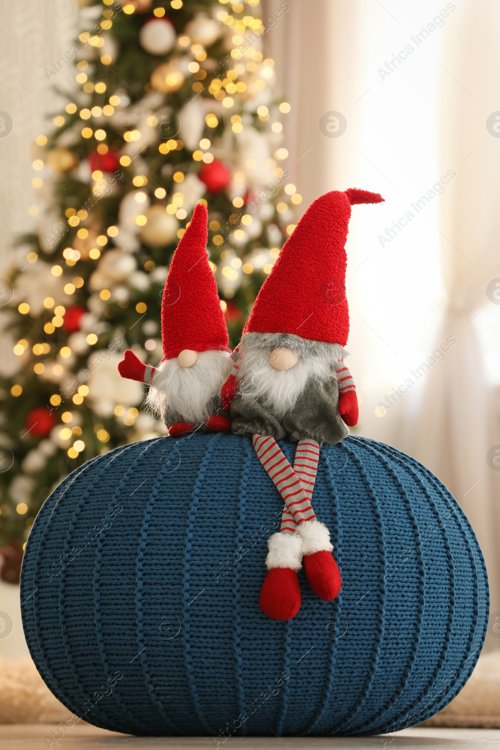 Photo of Cute Christmas gnomes on blue pouf in decorated room